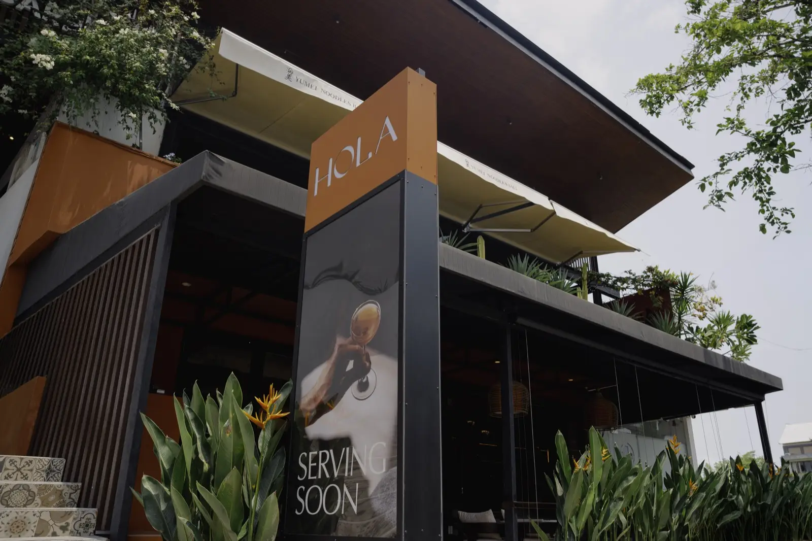 Hola's street sign with the logo and a Serving Soon poster