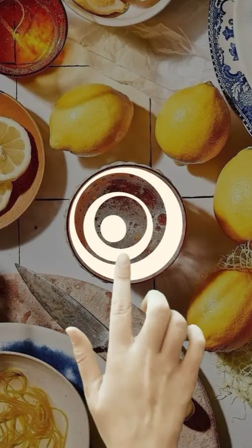 Reel frame: a hand taps the Hola symbol on a table of lemons and plates