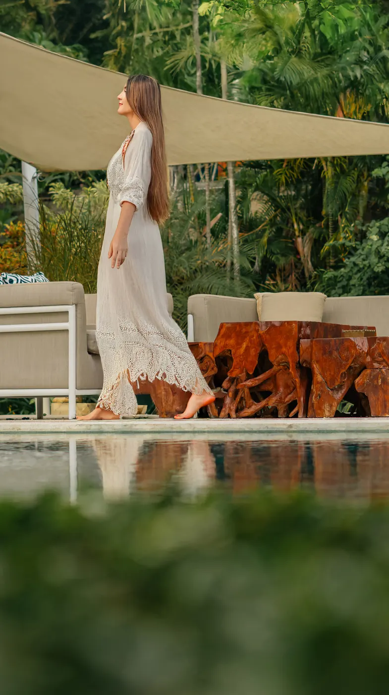 Guest in a long white dress walking past a poolside lounge