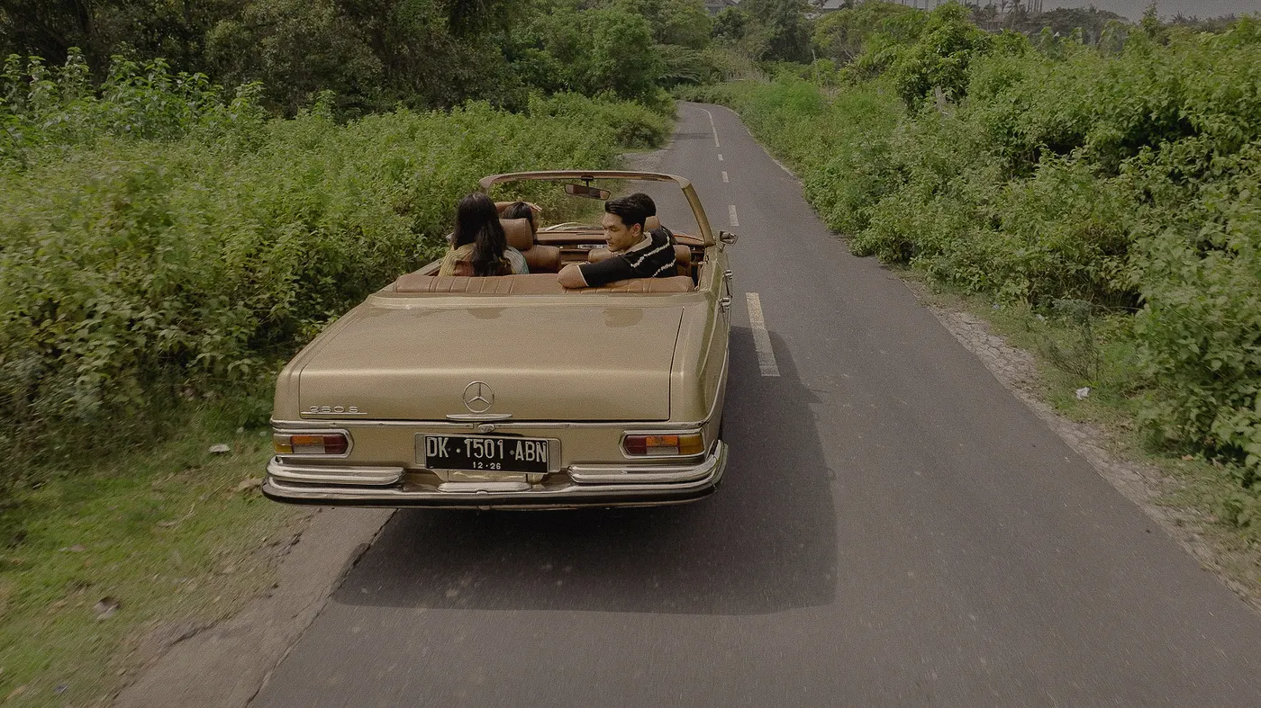 Cream convertible driving down a green country road